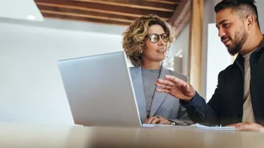 A woman and man talking in front of an open laptop
