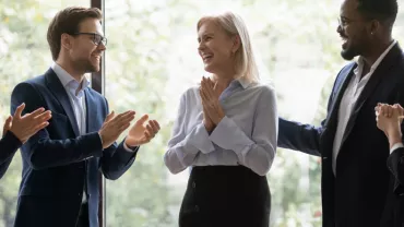 Group of colleagues applauding a smiling woman indoors.