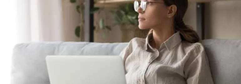 Woman with glasses using a laptop on a couch